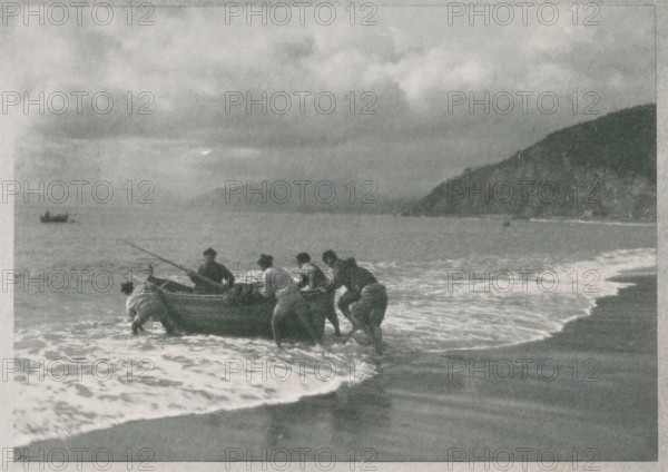 Seascape with fishermen, Italian fischer, page, photomechanical print, monogram: 'BX', photographer: W. Schmidt-Diehler, cliché maker: unknown, c. 1898 - in or before 1903, paper, autotypie, height 130 mm x width 125 mm, fisherman, sea (seascape), A grayscale scene of a shoreline with a group of people pushing a small boat from shallow surf toward the beach, their clothing appearing dark against the lighter foam of the waves; the boat sits at the waterline with a long pole extending from it, and another small vessel is visible farther out on the water; the sky above is filled with heavy, textured clouds, and a dark, sloping landmass frames the right side of the horizon while gentle waves wash onto the sand in the foreground.