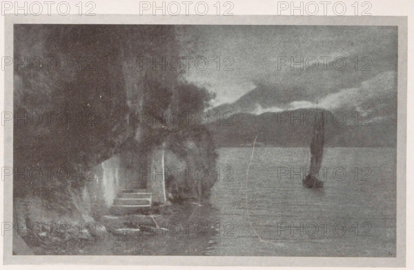 Am Gardasee, View of Lake Garda, page, photomechanical print, monogram: 'BX', inscription: 'Photographische Mitteilungen XL', photographer: A. Richter, Brescia (province), cliché maker: unknown, c. 1898 - in or before 1903, Lombardy, paper, autotype, height 120 mm x width 125 mm, lake, Lago di Garda, A grainy monochrome scene showing a shoreline with a small set of stone steps leading down to the water, dense dark foliage and tree trunks along the left edge, a stretch of calm water extending across the middle, and a small sailboat with a tall dark sail positioned on the water toward the right, under a sky filled with layered clouds and distant low hills on the horizon.