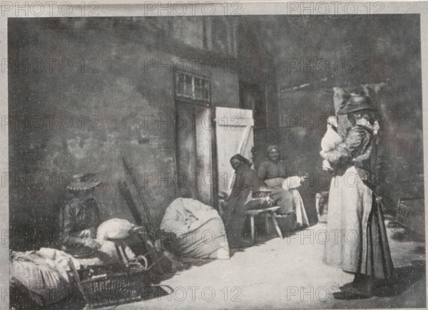Gänse rupfen, Plucking geese, page, photomechanical print, inscription: 'Berlin', monogram: 'BX', inscription: 'Photographische Mitteilungen XL', photographer: Hildegard Lehnert, cliché maker: unknown, c. 1898 - in or before 1903, paper, autotypie, height 128 mm x width 176 mm, geese (domestic waterbirds), A grainy black and white street scene shows a tall wall with a doorway partly covered by a half-open door and a small window above it, against which several people and piles of large wrapped bundles are arranged; on the left a seated figure wears a wide-brimmed hat and sits beside sacks and a basket, near a person bent over the bundles, while toward the center two seated women are positioned on simple stools with one facing forward and the other turned slightly, and on the right a standing woman wearing a long skirt and a coat with a hood or head covering holds a bundled child against her chest.