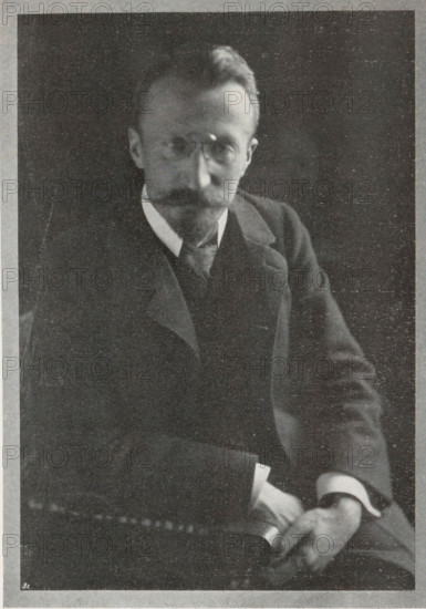 Field camera, page, photomechanical print, c. 1898 - in or before 1903, paper, autotype, height 76 mm x width 133 mm, camera, photography, A black-and-white portrait of a seated man wearing a dark suit with a vest and a light-colored shirt collar, showing a mustache and beard, round glasses, neatly combed hair, and his hands resting in his lap while holding a rolled object.