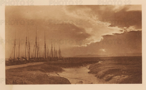 Landscape with a harbor and a stormy sky, A Stormy Evening, page, photomechanical print, photographer: Lionel C. Bennett, cliché maker: Photochrome Engraving Co., New York (city), printer (person): Walter L. Colls (possibly), c. 1895 - in or before 1900, printer (person), North America, paper, photoaquatint, height 112 mm x width 193 mm, behind semi-transparent cover., landscapes, harbor, A sepia-toned landscape showing a cluster of tall masts and rigging of boats lined along the left shoreline, a flat expanse of water or marsh stretching to the right, low grassy banks and winding muddy channels in the foreground, and a sky filled with heavy, layered clouds with lighter breaks near the horizon.