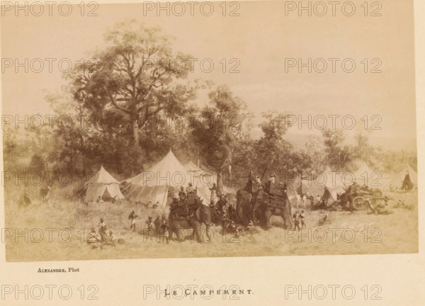 Le Campement, Photo reproduction of Le Campement by Jean Baptiste Robie, photograph, reproduction, page, photographer: Alexandre, after painting by Jean Baptiste Robie, c. 1878 - in or before 1883, paper, albumen print, height 113 mm x width 182 mm, behind cover., tent-camp, hunt, predatory animals (fox, lion), A wide sepia-toned scene shows a campsite set at the edge of a wooded area with tall trees rising behind a row of canvas tents of varying shapes and sizes; in front of the tents people move about while figures ride and lead pack animals loaded with gear, and other people stand or sit on the grassy ground, with clusters of activity near the animals and tent openings.