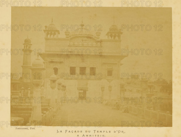 La Façade du Temple d'Or, a Amritsir, View of the Harmandir Sahib in Amritsar, photograph, page, photographer: Alexandre, Amritsar, c. 1880 - in or before 1885, Alexandre, photographer, paper, albumen print, height 132 mm x width 177 mm, behind cover., temple, shrine, non-Christian religions, Harmandir Sahib, A faded sepia photograph of a large ornate building with domed roofs and decorative turrets set behind a foreground walkway with low balustrades, showing arched windows and recessed doorways on the building facade, a tall slender tower with a small dome visible to the left, layered rooflines with projecting eaves and sculpted parapets, stone finials and small pavilion-like structures on the roof, and a broad open courtyard or approach leading up to the main entrance.
