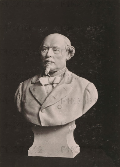 Buste of Achille Testelin, Buste du Sénateur A. Testelin, par MA Darcq, Statuaire, page, photomechanical print, inscription: 'Le Nord Contemporain, Revue Artistique', inscription: 'Journal le Nord Contemporain, No 24, année 1882.', photographer: NC, cliché maker: Ferrand, Lille, c. 1877 - in or before 1882-12-31, paper, collotype, photoprint, height 226 mm x width 164 mm, Print on third unnumbered page after page 384., Person, Achille Testelin, piece of sculpture, reproduction of a piece of sculpture, historical persons, A grayscale bust of an older man displayed against a dark background, showing his head and shoulders mounted on a pedestal; he has a receding hairline with hair at the sides, a mustache and a goatee, and a composed facial expression; he is depicted wearing a double-breasted coat with wide lapels, a bow at the collar, and a vest beneath, with visible buttons and tailored seams; the sculpture rests on a carved pedestal with smooth curved sides.