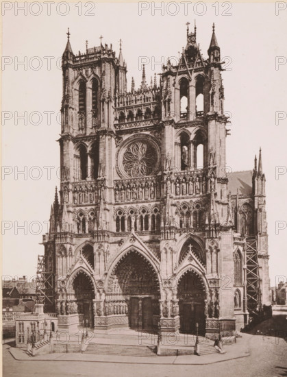 Le Cathédrale d'Amiens, vue générale extérieure, View of the Notre-Dame of Amiens, page, photomechanical print, inscription: 'Journal le Nord Contemporain, No 25, année 1883.', inscription: 'Le Nord Contemporain, Revue Artistique & Archéologique', photographer: NC, Amiens, cliché maker: Nemdein, Paris, c. 1878 - in or before 1883-01-20, NC, Nemdein, photographer, cliché maker, paper, collotype, photoprint, height 230 mm x width 175 mm, Print on third unnumbered page after page 16., church (exterior), Notre-Dame d'Amiens, A sepia-toned photograph of a Gothic cathedral facade showing twin towers with pointed spires, ornate stone carvings, arched doorways, a large circular rose window with radiating tracery, rows of sculpted figures in niches, decorative pinnacles and buttresses, scaffolding visible on one side, wide stone steps leading up to the entrance, lamp posts on the landing, and surrounding low buildings at the edges of the frame.