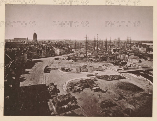 Dunkerque, Vue Générale, View of Dunkirk, page, photomechanical print, inscription: 'Le Nord Contemporain, Revue Pittoresque', photographer: NC, Dunkirk, c. 1878 - in or before 1883-02-20, paper, collotype, photoprint, height 165 mm x width 219 mm, Print on fifth unnumbered page after page 48., prospect of city, town panorama, silhouette of city, A wide waterfront scene shows a harbor filled with tall ships with masts and rigging clustered along the quay, adjacent to rows of multi-story buildings with pitched roofs and chimneys; an open cobblestone square in the foreground contains stacked crates and covered bundles, horse-drawn carts, and a curved roadway leading toward the docks, while a bridge spans a waterway near a small building at the edge of the quay and a distant tower rises above the town skyline.