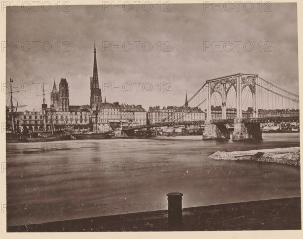 Rouen, Le Pont Suspendu, View of the suspension bridge in Rouen, page, photomechanical print, inscription: 'Le Nord Contemporain, Revue Pittoresque', inscription: 'Journal le Nord Contemporain, No 30, année 1883.', photographer: NC, c. 1878 - in or before 1883-04-05, paper, collotype, photoprint, height 169 mm x width 219 mm, Print on fifth unnumbered page after page 96., prospect of city, town panorama, silhouette of city, suspension bridge, A sepia-toned riverside scene showing calm water in the foreground and a city skyline along the far bank, with a large iron suspension bridge spanning from right to center, ornate towers and cables visible, multi-story buildings lining the riverbank behind the bridge, tall cathedral spires rising above the rooftops toward the left, masts and rigging of docked ships near the left edge, stone bridge piers and quay structures at the waterline, and a bollard silhouetted on the near edge of the riverfront.