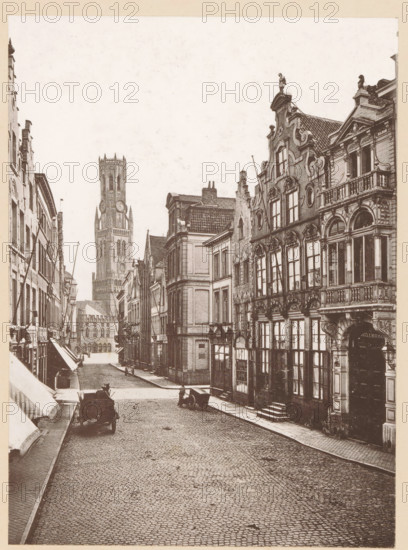 Bruges, La Rue Flamande, View of the Rue Flamande in Bruges, page, photomechanical print, inscription: 'Le Nord Contemporain, Revue Artistique & Archéologique', inscription: 'Journal le Nord Contemporain, No 32, année 1883.', photographer: NC, c. 1878 - in or before 1883-05-05, paper, collotype, photoprint, height 222 mm x width 162 mm, Print on third unnumbered page after page 128., street, A narrow cobbled street lined with tall, ornate buildings on both sides, featuring decorative facades, arched windows, balconies, and sculpted rooflines; a tall tower with a clock face rises in the distance, flanked by other stone structures; a few horse-drawn carts and a person near one cart are visible on the street, and awnings extend from some shopfronts along the left side.