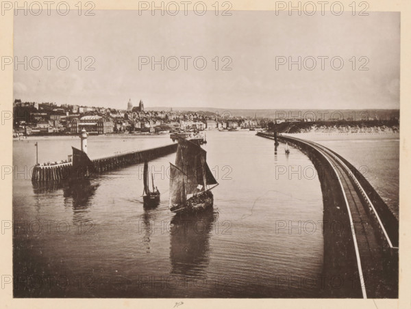 View of Boulogne-sur-Mer, Boulogne-sur-Mer, Vue Générale, page, photomechanical print, inscription: 'Le Nord Contemporain, Revue Artistique & Archéologique', inscription: 'Journal le Nord Contemporain, No 34, année 1883.', photographer: NC, c. 1878 - in or before 1883-06-05, paper, collotype, photoprint, height 164 mm x width 218 mm, Print on fifth unnumbered page after page 160., prospect of city, town panorama, silhouette of city, coastal structures, A sepia-toned waterfront scene shows calm water reflecting boats with tall sails in the foreground, a curved railway embankment running along the right side toward the distance, and a timber breakwater with a small lighthouse structure on the left. Along the far shore a dense cluster of buildings rises behind the waterfront, including larger domed and towered structures, with a low horizon and open sky above.