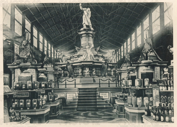 View of the section of Belgian breweries at the Antwerp World Exhibition in 1894, Collectivité des Brasseurs Belges, Exposition Universelle d'Anvers 1894, page, photomechanical print, photographer: Charles Bernhoeft, Antwerp, cliché maker: Charles Bernhoeft, Luxembourg (Belgian province), 1894, Charles Bernhoeft, photographer, cliché maker, paper, collotype, photoprint, height 153 mm x width 216 mm, beer, ale, brewer, world fair, world exhibition, World Exhibition 1894 (Antwerp), Period, 1894-05-05 - 1894-11-05, A large indoor scene shows a central raised monument with a tall column topped by a statue of a standing figure holding a long pole, surrounded by sculpted figures of children and animals on a multi-tiered base; flanking the monument are decorative urns with tall plants and ornate architectural elements, while symmetrical staircases lead up to the platform and are lined by balustrades and roped posts; the space is set inside a high hall with a visible roof structure of girders ...