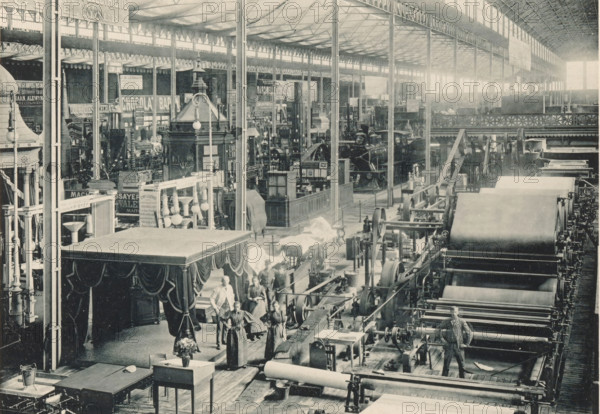 Fabrication de Papier, De Naeyer et Cie, View of a setup of the paper factory of De Naeyer & Cie at the Antwerp World Exhibition in 1894, Exposition Universelle d'Anvers 1894, page, photomechanical print, photographer: Charles Bernhoeft, Antwerp, cliché maker: Charles Bernhoeft, Luxembourg (Belgian province), 1894, Charles Bernhoeft, photographer, cliché maker, paper, collotype, photoprint, height 153 mm x width 216 mm, workshop interior, paper (writing material), world fair, world exhibition, World Exhibition 1894 (Antwerp), Period, 1894-05-05 - 1894-11-05, A large interior space with a high glass roof supported by slender metal columns and beams contains rows of industrial machinery with large cylindrical rollers and belts on a long assembly line, alongside display booths and ornate structures with decorative drapery and carved details; several people stand near the machines and booths, some wearing aprons or work clothes, and a man stands beside one of the large rollers; the foregro...