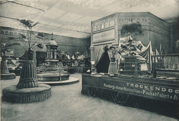 View of the maritime Hamburg part of the Antwerp World Exhibition in 1894, Section Maritime Hambourgeoise, Exposition Universelle d'Anvers 1894, page, photomechanical print, photographer: Charles Bernhoeft, Antwerp, cliché maker: Charles Bernhoeft, Luxembourg (Belgian province), 1894, Charles Bernhoeft, photographer, cliché maker, paper, collotype, photoprint, height 152 mm x width 222 mm, Print on third unnumbered page after page 38., counter, shop, couch, sofa, settee, world fair, world exhibition, World Exhibition 1894 (Antwerp), Period, 1894-05-05 - 1894-11-05, An indoor exhibition space captured in a monochrome photograph shows ornate architectural decoration along the upper walls and a high ceiling with a grid of skylights casting soft light. Large potted palm plants are arranged on round, upholstered pedestal seats with fluted skirts and tufted tops scattered across the floor. In the center area a circular fountain or basin with surrounding railings and steps is visible, topped ...