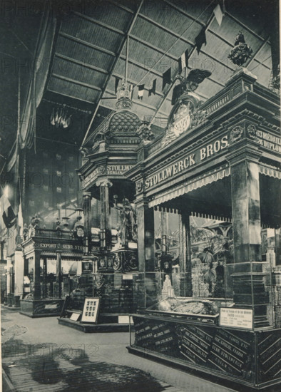 View of the food section of the Belgian part of the Antwerp World Exhibition in 1894, Section Belge, Groupe de l'Alimentation, Exposition Universelle d'Anvers 1894, page, photomechanical print, photographer: Charles Bernhoeft, Antwerp, Luxembourg (Belgian province), 1894, paper, collotype, photogravure, height 215 mm x width 152 mm, Print on third unnumbered page after page 114., counter, shop, industries, food, drink, stimulants, world fair, world exhibition, World Exhibition 1894 (Antwerp), Period, 1894-05-05 - 1894-11-05, A large indoor scene shows ornate exhibition booths with heavy decorative architecture, domed and columned structures, sculpted figures, and carved ornamentation; a prominent canopy with fringe hangs over one display and an eagle sculpture sits atop a decorated crest; flags hang from the high rafters of a vaulted ceiling and small pennants drape across the upper space; glass display cases contain objects and are set on raised platforms while framed items rest on ea...