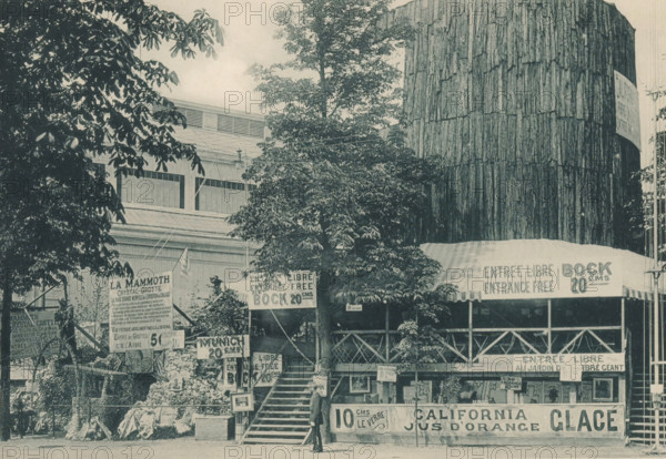 View of a tree trunk at the Antwerp World Exhibition in 1894, Arbre de Californie, Exposition Universelle d'Anvers 1894, page, photomechanical print, photographer: Charles Bernhoeft, Antwerp, cliché maker: Charles Bernhoeft, Luxembourg (Belgian province), 1894, Charles Bernhoeft, photographer, cliché maker, paper, collotype, photoprint, height 153 mm x width 216 mm, trees, world fair, world exhibition, World Exhibition 1894 (Antwerp), Period, 1894-05-05 - 1894-11-05, A wide scene shows a multi-level wooden and fabric pavilion partially obscured by large leafy trees, with a tall cylindrical structure covered in vertical wooden slats rising on the right. A staircase leads up to a covered porch area with a striped awning and lattice railing, and a man in a suit and hat is standing near the base of the steps. Rock formations and decorative plants are arranged near the stairs, and several freestanding signboards are positioned around the entrance area. The building behind the trees features...