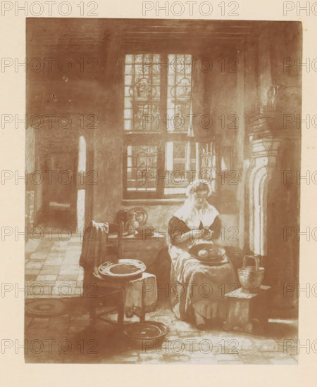 Photo reproduction of a painting of a woman peeling potatoes in a kitchen by Willem Linnig (II), photograph, reproduction, page, photographer: Alexandre van Antro, after print by Willem Linnig (II), c. 1891 - in or before 1896, Willem Linnig (II), after print by, paper, daylight collodion silver print, height 148 mm x width 117 mm, adult woman, kitchen, potatoes, A monochrome image showing an interior room with a tall window made of small panes and decorative circular patterns, light falling through it onto a seated woman in historical dress wearing a white cap and apron, who is focused on an object in her hands while holding a bowl on her lap; around her are household items including a table with plates and a pitcher, a small stool with a metal bucket, draped cloths, and floor tiles in a checker pattern, with an arched doorway visible to the left and a carved architectural element on the right.