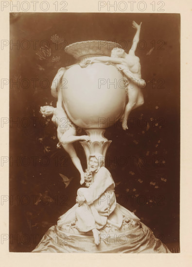 Vase depicting the temptation of Saint Anthony, by A. Magni, photograph, page, photographer: Alexandre van Antro, c. 1891 - in or before 1896, paper, daylight collodion silver print, height 171 mm x width 121 mm, piece of sculpture, reproduction of a piece of sculpture, vase, ornament, the erotic visions of St. Antony Abbot: he is tempted by (naked) women, but drives them off by praying, or by showing them a crucifix, A tall ornate object resembling a large decorative urn sits at the center, supported by a fluted pedestal and a draped base. Sculpted human figures cling to and emerge from the urn: one semi-reclining figure wraps around the upper rim with an arm extended upward, another figure hangs from the side with legs dangling, and a seated robed figure rests at the pedestal with a contemplative expression and folded hands. The surface of the urn is smooth and rounded with a scalloped rim on top. The background is dark with faint floral and bird-like shapes. The photograph has a war...