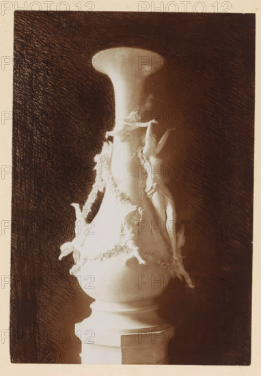 Vase, depicting an allegory of abundance, by Grossi, photograph, page, photographer: Alexandre van Antro, c. 1891 - in or before 1896, paper, daylight collodion silver print, height 171 mm x width 117 mm, piece of sculpture, reproduction of a piece of sculpture, Abundance, 'Abondanza', 'Abondanza maritima' (Ripa), ornament, A tall ornate vase with a flared rim sits on a multi-tiered pedestal, its surface light in tone against a dark, heavily hatched background. Decorative sculpted figures climb and cling to the vase, including a prominent partially draped female figure with arms raised and flowing hair, smaller reclining and reaching figures entwined along the vase's side, and floral or garland-like sculptural details cascading downward. The image shows strong contrasts of light and shadow emphasizing the smooth curves of the vase and the three-dimensional forms of the figures. The edges of the photograph are framed by a lighter border.
