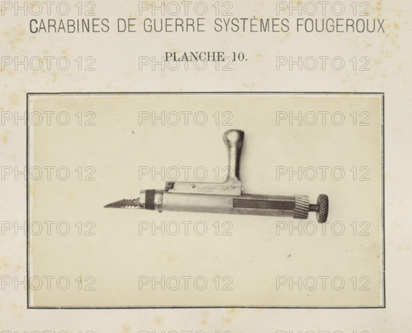 Safety catch of a rifle, photograph, page, inscription: 'Carabines de guerres systèmes Fougeroux', number: 'Planche 10.', photographer: Edouard Magis, Liège, c. 1857 - in or before 1867, paper, albumen print, height 158 mm x width 96 mm, Image in section at the back., firearms: rifle, A sepia-toned page shows a rectangular framed area containing a photographed metal tool positioned horizontally near the top of the framed area; the tool has a rounded vertical handle rising from its body, a blade with serrated edge at one end, and a cylindrical knurled adjustment knob at the opposite end, with visible screws and machined surfaces and slight shadows on the paper background.