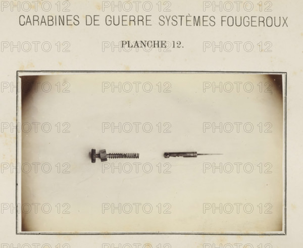 Two parts of the safety catch of a rifle, photograph, page, inscription: 'Carabines de guerres systèmes Fougeroux', number: 'Planche 12.', photographer: Edouard Magis, Liège, c. 1857 - in or before 1867, paper, albumen print, height 158 mm x width 96 mm, Image in section at the back., firearms: rifle, A sepia-toned page with a rectangular bordered area containing two small metal objects centered near the top of the bordered area; the left object is a short cylindrical piece with textured knobs, a coiled spring extending from it, and a small threaded section, while the right object is a slender metal rod attached to a short hollow cylindrical housing with a pointed tip; the page shows slight spotting and aged discoloration around the edges.