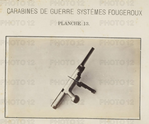 Safety catch of a rifle, photograph, page, inscription: 'Carabines de guerres systèmes Fougeroux', number: 'Planche 13.', photographer: Edouard Magis, Liège, c. 1857 - in or before 1867, paper, albumen print, height 158 mm x width 96 mm, Image in section at the back., firearms: rifle, A rectangular page with a centered light background and a thin double-lined border contains a photograph of a metallic mechanical piece placed diagonally, showing a cylindrical shaft with a rounded knob at one end, a bolt-like threaded tip at the other, and a perpendicular handle with a textured grip and a small flat blade projecting from near its base; the page shows light age spots and slight discoloration.