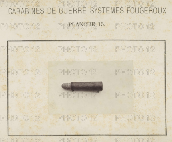 Bullet, photograph, page, inscription: 'Carabines de guerres systèmes Fougeroux', number: 'Planche 15.', photographer: Edouard Magis, Liège, c. 1857 - in or before 1867, paper, albumen print, height 55 mm x width 88 mm, Image in section at the back., ammunition, A rectangular aged paper page with a thin double-lined border and mottled brown spotting, a centered pale rectangular photograph mounted slightly above the middle, and a single dark cylindrical projectile with a rounded grooved tip resting horizontally on the photograph.