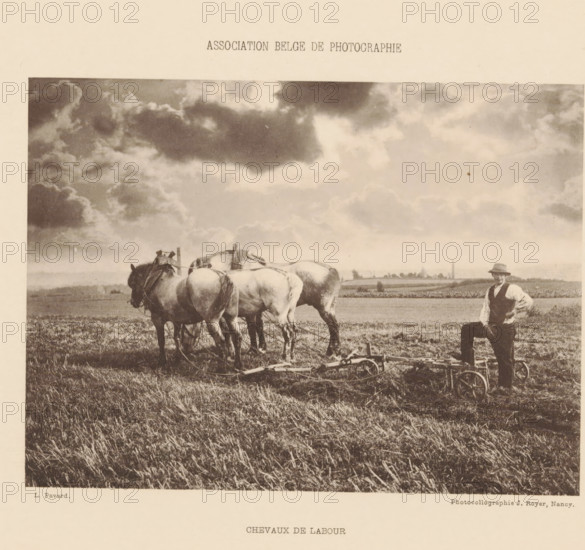 Farmer in the field with work horses, Chevaux de labour, page, photomechanical print, inscription: 'Association Belge de photographie', photographer: L. Pavard, cliché maker: Jules Royer, Nancy, c. 1893 - in or before 1898, paper, collotype, photoprint, height 116 mm x width 157 mm, farmers, horse, A sepia-toned photograph showing a rural field under a sky filled with large, billowing clouds, a team of heavy horses standing harnessed together with their rears toward the viewer, ploughing equipment resting on the ground behind them, and a man wearing a hat and vest standing with one foot on the equipment at the edge of the field.