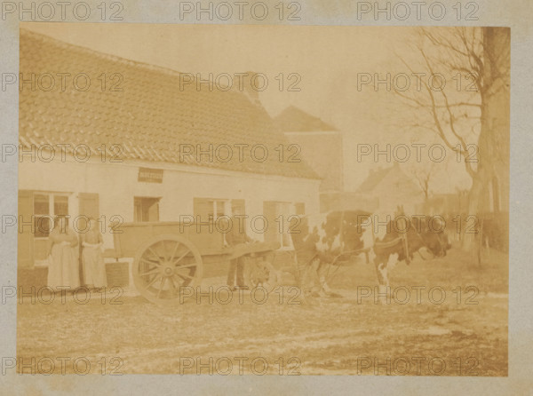 Farmer with a cart pulled by a cow, photograph, page, c. 1888 - in or before 1893, photographer, paper, albumen print, albumendruk, height 120 mm x width 168 mm, farmers, cow, two-wheeled vehicle drawn by one animal, A sepia-toned photograph showing a single-story building with a tiled roof and shuttered windows, a wooden cart with large spoked wheels positioned in front of the building, two women standing side by side near a window wearing long dresses, a man near the cart dressed in a coat and hat, a pair of cows hitched to the cart, and bare trees visible along the right edge of the scene.