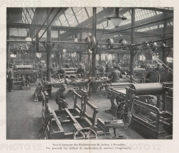 View of a workshop for the construction of printing equipment in the Société anonyme des Établissements H. Jullien in Brussels, Société anonyme des Établissements H. Jullien, à Bruxelles., Vue générale des ateliers de construction de material d'imprimerie, page, photomechanical print, Brussels, cliché maker: Jean Malvaux, c. 1906 - in or before 1911, Jean Malvaux, photographer, cliché maker, paper, autotypie, height 149 mm x width 188 mm, Print on second and third unnumbered page after page 176., tools, implements of printer, A large industrial interior with rows of machinery and workbenches filling the floor, overhead beams and pulleys stretching across the space, large windows in the roof letting light in, hanging lamps suspended from the ceiling, multiple workers at benches operating tools and machines, visible gears, wheels, belts, and mechanical frames, tall support columns rising through the workspace, scattered tools and parts on the benches, and a foreground view of machine fra...