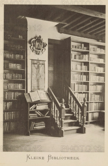 Interior of the library of Christoffel Plantijn, Small library, page, photomechanical print, maker: Joseph Maes, c. 1881 - in or before 1886, paper, collotype, photoprint, height 160 mm x width 110 mm, Print on second unnumbered page after page 136., study, 'studiolo', library, A monochrome photograph of an interior showing wooden bookshelves filled with books on both sides of a short carved staircase with turned balusters and newel posts; a small lectern or bookstand beside the staircase holds an open large book and has additional books on its lower shelves; a narrow vertical hanging image is mounted on the wall above the lectern and an ornamental crest is displayed above it; exposed ceiling beams run across the top of the room and a dark doorway is visible behind the staircase.