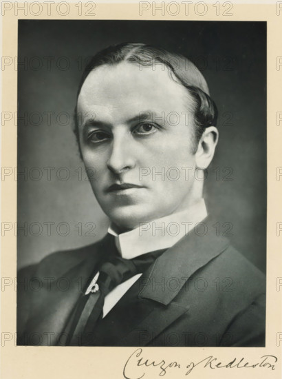 The right honorable lord Curzon of Kedleston, photograph, page, inscription: '55, Baker St, London, W.', annotation, photographer: Elliott & Fry, c. 1893 - c. 1903, paper, carbon print, height 227 mm x width 171 mm, Person, George Curzon, historical persons (portraits and scenes from the life) ((full) bust portrait), A black and white portrait of a man shown from the shoulders up wearing a dark suit jacket, a high white collar, and a dark tie with a decorative pin. He has a smooth, pale complexion, neatly combed hair with a waved part, and an expressionless face with slightly downturned lips. The background is plain and darker than his face, and a narrow light-colored border surrounds the photograph.