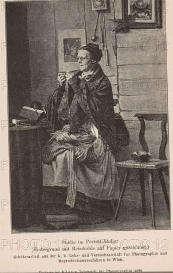 Studio portrait of an unknown seamstress, page, photomechanical print, inscription: 'Studio im Portät-Atelier, (Hintergrund mit Reisskohle auf Papier gezeichnet.)', maker: KK Lehr- und Versuchsanstalt für Photographie, c. 1885 - in or before 1890, paper, autotypie, height 138 mm x width 95 mm, Print on the twenty-first unnumbered page after page 400., historical persons - BB - woman, sewing, An older woman sits on a bench wearing layered garments and a shawl, holding a small object close to her face with both hands and looking slightly to the side, her hair pulled back and she wears glasses; beside her a small table holds a book and other objects, and a simple wooden chair stands nearby with a bowl-like item on its seat; the background shows a wall with framed pictures and hanging objects, and the scene is rendered in a monochrome, stippled or engraved style.