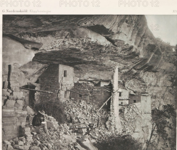 Befästad klippremna ledane till Balcony House, View of an entrance to the Balcony House in Mesa Verde National Park, page, photomechanical print, name, number: 'Fig. 42.', photographer: Gustaf Nordenskiöld (possibly), Mesa Verde National Park, cliché maker: Angerer & Göschl, C., Vienna, c. 1891 - in or before 1893, clichémaker, North America, Lower Austria, Colorado, paper, autotypie, height 201 mm x width 106 mm, ruin of a dwelling, house, castle, cave-dwelling, A grayscale photograph shows a rocky cliff overhang with irregular textured rock surfaces and ledges, beneath which a cluster of stone and adobe structures sits in various states of ruin with exposed walls, a tall narrow chimney, and piles of rubble and scattered masonry; a person wearing a hat and dark clothing is seated on a low stone wall near the rubble holding an open book or object, and wooden beams and planks lean against and span parts of the ruins, with sparse vegetation and small trees visible at the cliff edge.