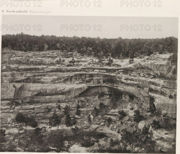 View of a cliff dwelling, Kodak House, in Mesa Verde National Park, The Kodak House, page, photomechanical print, number: 'I', inscription: 'G. Nordenskiöld: Klippboningar.', photographer: Gustaf Nordenskiöld, Mesa Verde National Park, cliché maker: Librairies-Imprimeries Réunies (Ancienne Maison Quantin), Paris, c. 1891 - in or before 1893, North America, Colorado, paper, photoaquatint, height 187 mm x width 240 mm, ruin of a dwelling, house, castle, A wide grayscale photograph showing layered rock formations with horizontal striations and ledges, sparse vegetation growing on and between the rocks, a tree line along the top edge, uneven rocky surfaces with cracks and boulders, an overhanging rock shelf creating a shallow recess, and lighter sky above the distant treeline.