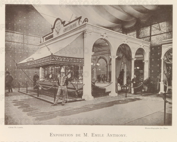 Exposition de M. Emile Anthony, Expositie van de goudsmid Emile Anthony tijdens de wereldtentoonstelling te Antwerpen, page, photomechanical print, photographer: Th. Lantin, Antwerp, clichémaker: Joseph Maes, 1894, paper, collotype, light print, height 160 mm x width 220 mm, jeweler, goldsmith, silversmith, world fair, world exhibition, exhibition, show, A large indoor scene shows a decorative pavilion with arched openings, fluted columns with ornate capitals, and draped curtains inside the arches. A striped canopy extends from one side of the structure above a glass display counter filled with objects, and a rope barrier encircles the area. Several men in uniforms stand near the pavilion, one in front holding a long pole and another seated near the entrance. The background features patterned walls and a high ceiling with sweeping fabric drapery, and there are lamps and furniture visible through the arches. The floor in front of the pavilion has rectangular matting leading toward the s...