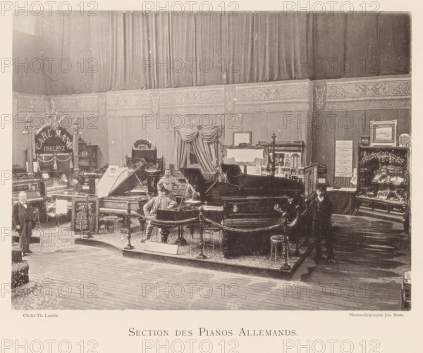 Exhibition of German pianos during the world exhibition in Antwerp, Section des Pianos Allemands, page, photomechanical print, photographer: Th. Lantin, Antwerp, cliché maker: Joseph Maes, 1894, paper, collotype, light printing, height 165 mm x width 220 mm, grand piano, world fair, world exhibition, exhibition, show, A sepia-toned interior scene showing a large room with tall draped curtains and an ornate frieze along the upper wall, filled with multiple grand pianos and other keyboard instruments arranged on a raised, carpeted platform bordered by decorative posts and chains; several men in period clothing are standing and sitting among the instruments, one seated at a piano with its lid open and another standing near the platform edge; display cabinets, decorative stands, and framed items occupy the back and side walls, and a wooden floor extends in front of the platform.