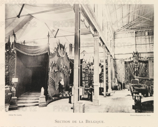 Section de la Belgique, Exhibition of Belgian weapons during the World Exhibition in Antwerp, page, photomechanical print, photographer: Th. Lantin, Antwerp, clichémaker: Joseph Maes, 1894, paper, collotype, photoprint, height 159 mm x width 219 mm, weapons, world fair, world exhibition, exhibition, show, A large indoor space with a high ceiling supported by visible beams and arched fabric drapery stretches across the top, with a row of tall columns and open archways running down the middle right, creating a corridor lined with decorative displays. On the left, a dark draped canopy with fringed trim covers a raised platform with steps leading up to it, flanked by ornamental posts topped with small finials and cylindrical objects on pedestals. Adjacent to the canopy, a tall ornate backdrop features radiating decorative elements, sculpted figures, and a bust on a pedestal, with a uniformed figure standing nearby. Further along the corridor, additional decorative panels and arch-like stru...