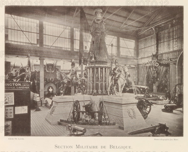 Exhibition of Belgian weapons during the World Exhibition in Antwerp, Section Militaire de Belgique, page, photomechanical print, photographer: Th. Lantin, Antwerp, clichémaker: Joseph Maes, 1894, paper, collotype, photogravure, height 160 mm x width 220 mm, weapons, world fair, world exhibition, exhibition, show, A large indoor exhibition space with tall windows and a high roof showing exposed beams and metal supports contains multiple displays of military equipment including cannons, ammunition, and wheeled artillery pieces arranged on wooden flooring and raised stone-like platforms; a central tall cylindrical structure decorated with vertical elements and topped with ornamental radial pieces stands prominently, flanked by two mounted figures in uniform on horses wearing decorative bridles and saddles; flags and banners hang around the perimeter and decorative fan-shaped arrangements and ladders are visible against the walls, while various smaller objects and framed panels are positi...