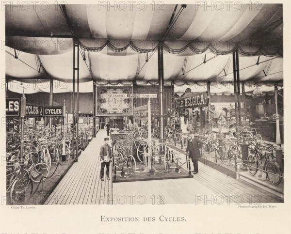Exposition des Cycles, Expositie van fietsen tijdens de wereldtentoonstelling te Antwerpen, page, photomechanical print, photographer: Th. Lantin, Antwerp, clichémaker: Joseph Maes, 1894, paper, collotype, light print, height 157 mm x width 220 mm, bicycle, world fair, world exhibition, exhibition, show, A large indoor exhibition space filled with rows of bicycles displayed on stands beneath a fabric ceiling with scalloped valances and decorative fringe, supported by tall slender columns and overhead rigging; wooden plank walkways run between the displays and a few men in period clothing stand among the bicycles, one near the foreground holding papers and another leaning on a rail, while ornate signs and framed panels hang above the exhibits and potted plants are placed near some of the displays.