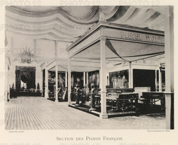 Section des Pianos Français, Exhibition of French pianos during the World Exhibition in Antwerp, page, photomechanical print, photographer: Th. Lantin, Antwerp, cliché maker: Joseph Maes, 1894, paper, collotype, light printing, height 160 mm x width 219 mm, grand piano, world fair, world exhibition, exhibition, show, An indoor exhibition space with a striped fabric ceiling draped in sweeping curves and a wooden plank floor; a series of columned booths and canopies occupy the area, each sheltering furniture and musical instruments including ornate pianos and carved statues; heavy curtains and decorative pediments frame openings at the back, and framed paintings hang on the inner walls of some booths; the scene shows a mix of dark and light tones with shadows cast by the canopy structures and various ornamental details on the furnishings.