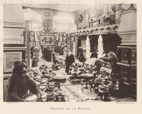 Section de la Russie, Exhibition of Russian fur products during the world exhibition in Antwerp, page, photomechanical print, photographer: Th. Lantin, Antwerp, cliché maker: Joseph Maes, 1894, paper, collotype, photoprint, height 160 mm x width 220 mm, spoils of the hunt, game, venison, world fair, world exhibition, exhibition, show, A large indoor scene shows an exhibition-like space filled with animal hides, fur garments, and stuffed animal figures arranged on platforms and tables. In the foreground a seated bear figure faces slightly toward the viewer with a bowl in front of it, surrounded by low round stools topped with patterned cushions and small carved objects. Further back there are more furry seated figures and standing animal forms placed on draped surfaces and rugs, with rows of hanging coats and long fur garments visible along the midground. The walls and partitions are decorated with large patterned textiles and banners, and sculpted animal heads and pelts are displayed o...