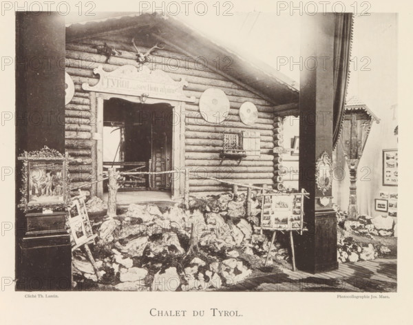 Chalet du Tyrol, Tyrolean chalet in the world exhibition in Antwerp, page, photomechanical print, photographer: Th. Lantin, Antwerp, cliché maker: Joseph Maes, 1894, paper, collotype, light printing, height 161 mm x width 219 mm, world fair, world exhibition, exhibition, show, log-cabin, A photograph of a rustic log facade with a peaked roof and a doorway framed by carved wood, mounted antlers above the entrance, circular plaques on the exterior wall, a small shuttered window with a decorative grille, and a rough rocky foreground with a simple wooden fence; an easel displaying mounted images stands among the rocks, an ornate framed painting rests nearby, and a tall carved column with decorative panels and a small roofed shrine is visible to the right, all within an interior space with wooden floorboards and vertical supporting beams.