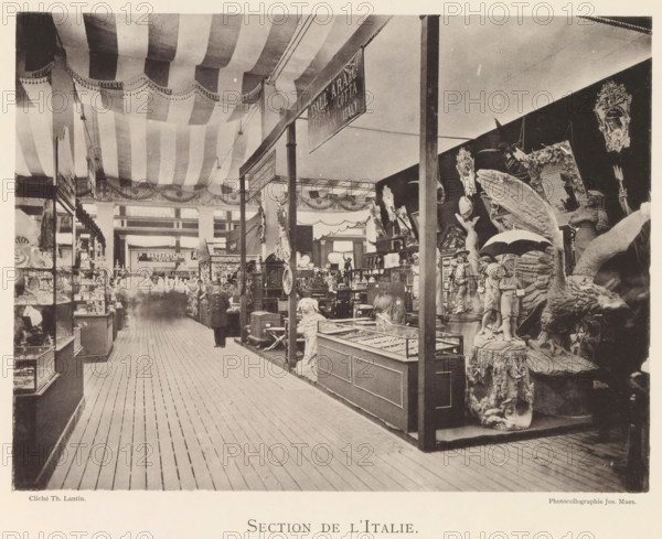 Section de l'Italie, Exhibition of Italian objects during the world exhibition in Antwerp, page, photomechanical print, photographer: Th. Lantin, Antwerp, cliché maker: Joseph Maes, 1894, Th. Lantin, Joseph Maes, photographer, cliché maker, paper, collotype, light printing, height 165 mm x width 220 mm, world fair, world exhibition, exhibition, show, A large indoor exhibition space with a wooden plank floor and a striped fabric ceiling draped across the top, supported by vertical posts that divide display areas; glass display cases and shelves line the left side and central aisles, while the right side features a dense arrangement of decorative sculptures and carved figures including a winged creature, a pair of child figures holding an umbrella, and various ornate frames and statues, all positioned on pedestals and platforms; a few blurred human figures are visible among the displays and a hanging rectangular sign is suspended from the ceiling structure.