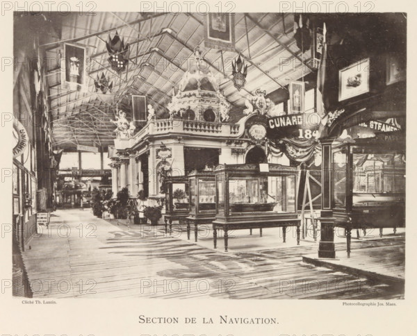 Section de la Navigation, Exhibition of ship models during the World Exhibition in Antwerp, page, photomechanical print, photographer: Th. Lantin, Antwerp, clichémaker: Joseph Maes, 1894, paper, collotype, photoprint, height 160 mm x width 220 mm, ship-model, world fair, world exhibition, exhibition, show, A large indoor exhibition hall with a high arched ceiling supported by visible metal trusses, decorative banners and shields hanging from the rafters, ornate classical architectural structures with sculpted figures and a domed pavilion, glass display cases on wooden legs arranged on a wooden plank floor, potted plants and small trees placed near the displays, framed pictures and additional banners mounted on the walls, a combination of open walkways and partitioned exhibition booths, and various decorative draperies and sculptural details throughout the space.