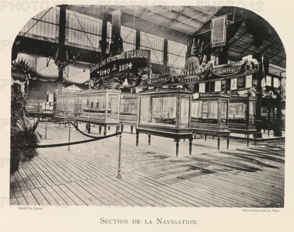 Exhibition of ship models during the World Exhibition in Antwerp, Section de la Navigation, page, photomechanical print, photographer: Th. Lantin, Antwerp, clichémaker: Joseph Maes, 1894, paper, collotype, photoprint, height 160 mm x width 218 mm, ship-model, world fair, world exhibition, exhibition, show, An indoor exhibition space with a high roof and large windows shows rows of glass display cases on ornate wooden legs containing model ships, a wooden plank floor with rope barriers supported by decorative posts, draped banners and decorative panels above the displays, tall vertical supports and hanging decorative elements, framed pictures and ornamental signage along the back, and potted plants visible at the left edge.