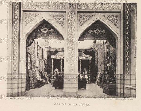 Exhibition of Persian objects during the World Exhibition in Antwerp, Section de la Perse, page, photomechanical print, photographer: Th. Lantin, Antwerp, clichémaker: Joseph Maes, 1894, paper, collotype, photoprint, height 160 mm x width 219 mm, world fair, world exhibition, exhibition, show, A sepia photograph of an arched storefront with two large pointed arches separated by a central decorative pillar, both arches framed by patterned borders and floral motifs. Inside the arches are hanging textiles with geometric patterns forming dark draped canopies, and beneath them are stacked rugs and folded fabrics displayed along the side walls. Wooden shelving units filled with boxes and small objects sit toward the back under scalloped awnings, and a few rolled carpets and folded textiles lean against the walls near the entrance. The floor is tiled and the lower walls show horizontal banding, while ornamental vertical panels with repeating floral designs flank the outer edges of the scene.