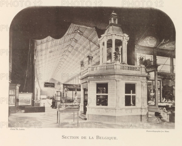 Exhibition of Belgian objects during the World Exhibition in Antwerp, Section de Belgique, page, photomechanical print, photographer: Th. Lantin, Antwerp, clichémaker: Joseph Maes, 1894, paper, collotype, photoprint, height 160 mm x width 220 mm, world fair, world exhibition, exhibition, show, A large interior space with a high vaulted ceiling composed of repeating trusses extends into the distance, framed by a rounded dark border at the top edges. In the foreground a multi-sided pavilion with balustraded upper railings and tall columns supporting a small domed cupola stands prominently, with hanging plants placed near its corners. Glass display cases and framed artworks are arranged along the floor area, and a few freestanding decorative streetlamp-like structures rise near the pavilion. Ornate painted panels with floral and bird motifs decorate a wall to the right, and tall windows admit light behind the decorative elements. Various small objects and fixtures are visible on tables an...