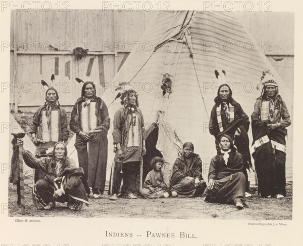 Indiens - Pawnee Bill, Group portrait of Pawnee in front of a tent at the world exhibition in Antwerp, page, photomechanical print, photographer: Th. Lantin, Antwerp, cliché maker: Joseph Maes, 1894, paper, collotype, photoprint, height 160 mm x width 219 mm, anonymous historical persons depicted in a group, in a group-portrait, indigenous peoples of North America, tepee, tipi, teepee, world fair, world exhibition, original inhabitants of America, A group of people posed in front of a large conical tent, with some standing and some seated on the ground; several wear feathered headdresses and patterned clothing, some have long hair in braids, and many wear long narrow chest adornments and beaded or fringed garments; one seated person at the left holds a long patterned staff or strap, and a child sits on the ground near the center; the tent shows vertical stitching and laces at its entrance, and a wooden fence or wall is visible behind the tent.