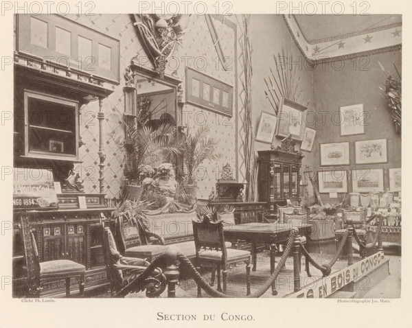 Exhibition of wooden furniture from Congo at the world exhibition in Antwerp, Section du Congo, page, photomechanical print, photographer: Th. Lantin, Antwerp, cliché maker: Joseph Maes, 1894, paper, collotype, light printing, height 160 mm x width 219 mm, world fair, world exhibition, exhibition, show, seating furniture, A room filled with ornate wooden furniture including carved chairs, a table, cabinets, and a large mirrored mantle, surrounded by framed pictures on patterned walls and decorative spears leaning against the corner, with potted plants and sculpted busts arranged on and around the furniture, a rope barrier suspended between posts in the foreground, and a ceiling border decorated with star motifs.