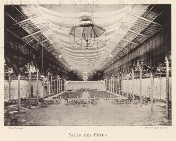 Interior of a banquet hall in Antwerp, Salle des fêtes, page, photomechanical print, photographer: Th. Lantin, Antwerp, printer (person): Joseph Maes, 1894, printer (person), paper, collotype, photoprint, height 160 mm x width 219 mm, public festivities, interior, representation of a building, A large indoor hall with a high vaulted ceiling draped with fabric swags and a central oversized chandelier suspended above rows of folding chairs arranged facing a raised platform at the far end; tall slender columns line both sides supporting decorative drapery and overhead trusses, with hanging globe lights spaced along the ceiling and smaller chandeliers mounted on poles near the aisles, while the floor appears bare and expansive in the foreground.