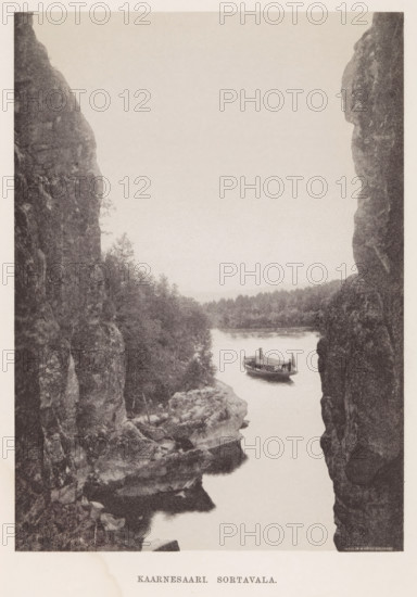 View of a steamboat launching from a spot between two rocks, Kaarnesaari. Sortavala, page, photomechanical print, photographer: Impi Backman, cliché maker: anonymous, printer (person): Weilin & Göös, c. 1888 - c. 1893, printer (person), paper, autotypie, height 224 mm x width 163 mm, trees, landscapes with waters, waterscapes, seascapes (in the temperate zone), steamship, motorship, rocks, Karelia, A narrow vertical view framed by tall rocky cliffs on either side reveals a calm river flowing between them with a small wooden boat floating near the center of the water, the boat showing a covered cabin and a single flag at its stern; dense treeline and low wooded hills line the far riverbank, and textured rock shelves and vegetation appear along the near cliff edges, all rendered in a monochrome, grainy photographic tone.